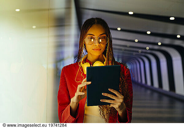 Young woman with braided hair using tablet PC in illuminated underground tunnel