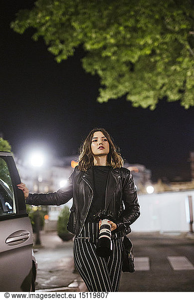 Young woman with camera at a car at night