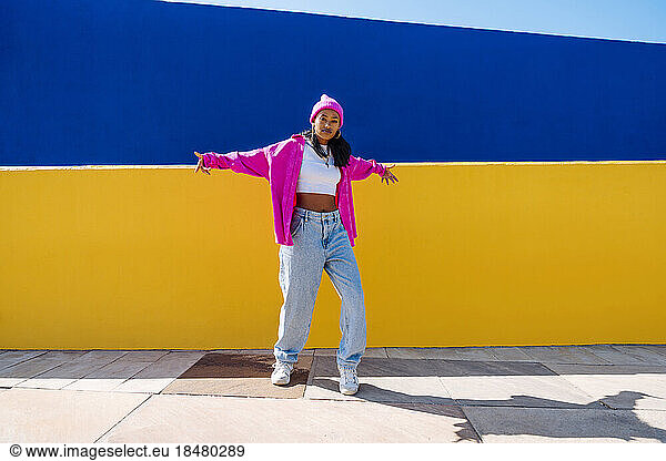Young woman with cool attitude dancing in front of two tone color wall