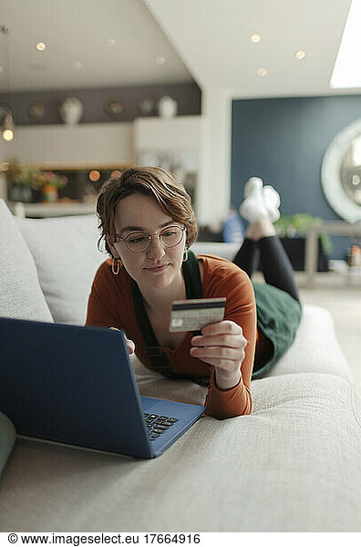 Young woman with credit card paying bills online at laptop on sofa