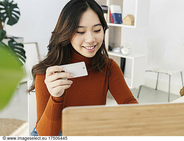 Young woman with credit card shopping online through laptop at home