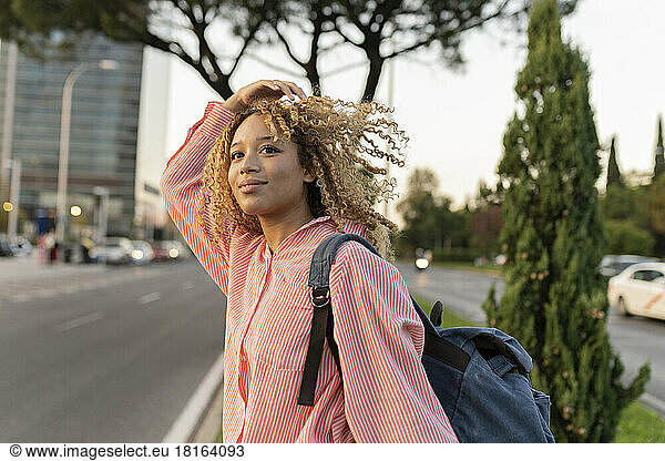 Young woman with curly blond hair carrying backpack crossing street