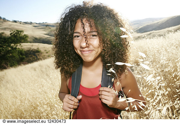 Young woman with curly brown hair hiking in urban park  smiling at camera.