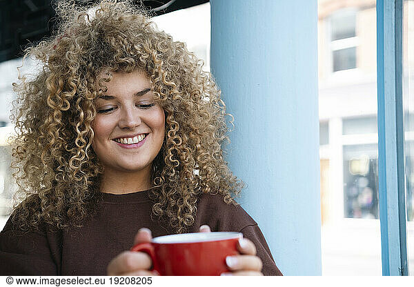 Young woman with curly hair holding coffee cup at cafe