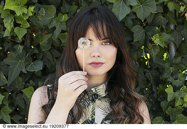 Young woman with dandelion flower in front of plants
