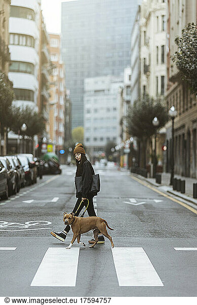 Young woman with dog crossing street in city