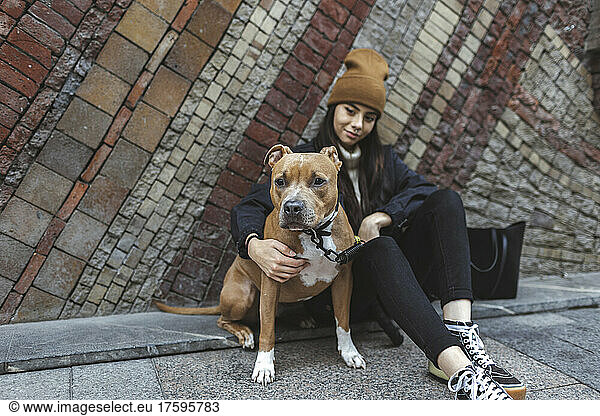 Young woman with dog sitting in front of wall