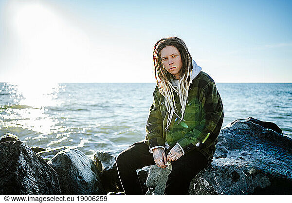 Young woman with dreadlocks sitting near seashore