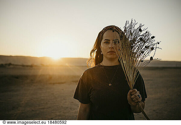 Young woman with dried plants in front of clear sky at sunset
