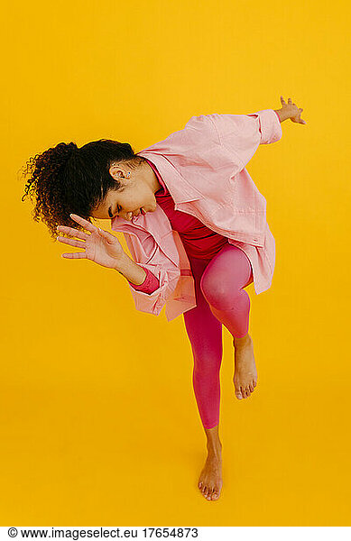 Young woman with eyes closed dancing against yellow background