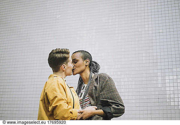 Young woman with eyes closed kissing girlfriend while standing against wall
