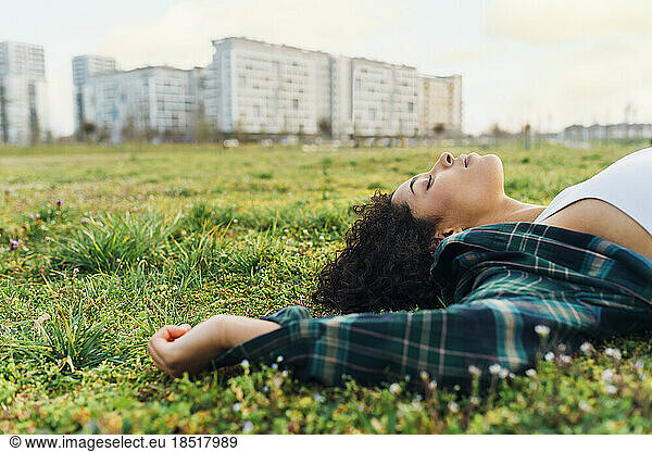 Young woman with eyes closed relaxing in grass at sunset