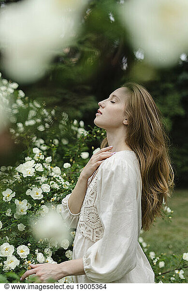 Young woman with eyes closed standing by white flower bush