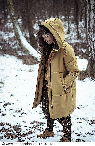 young woman with freckles & long curly hair smiles under hood in snow