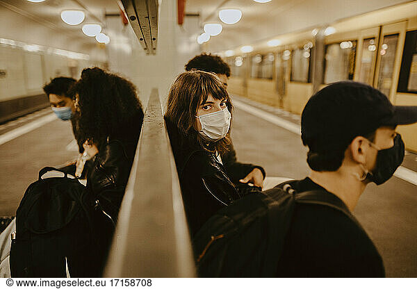 Young woman with friends sitting at subway station during pandemic