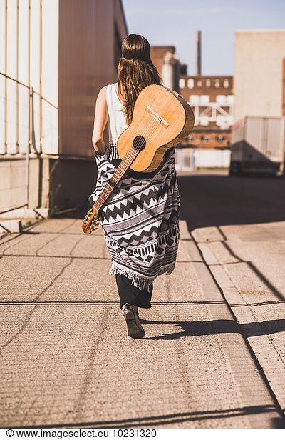Young woman with guitar on her back walking on street