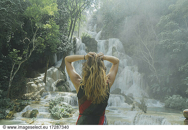 Young woman with hand in hair standing in front of Kuang Si waterfall in Luang Prabang  Laos