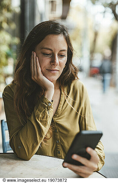 Young woman with hand on chin using smart phone in cafe