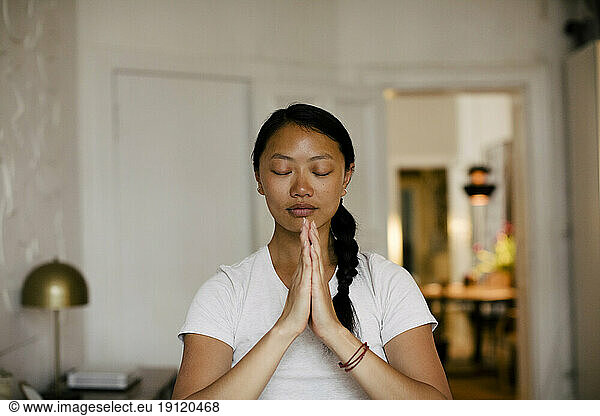 Young woman with hands clasped meditating at home
