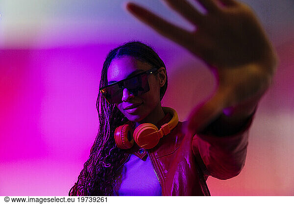 Young woman with headphones and sunglasses gesturing in illuminated tunnel