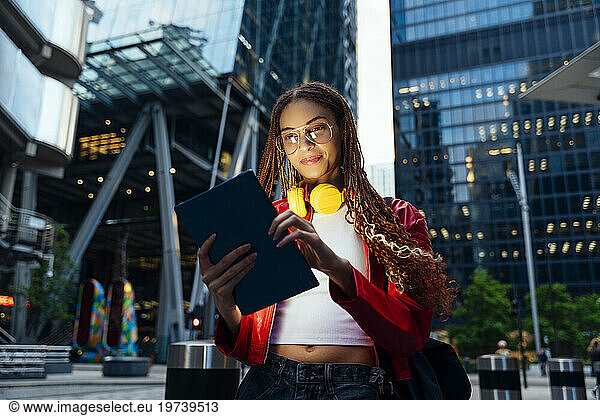 Young woman with headphones using tablet PC in city