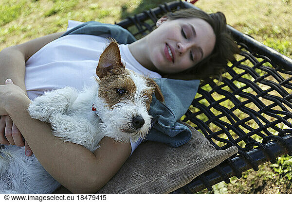 Young woman with Jack Russell Terrier lying on hammock in park