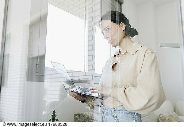 Young woman with laptop looking through window