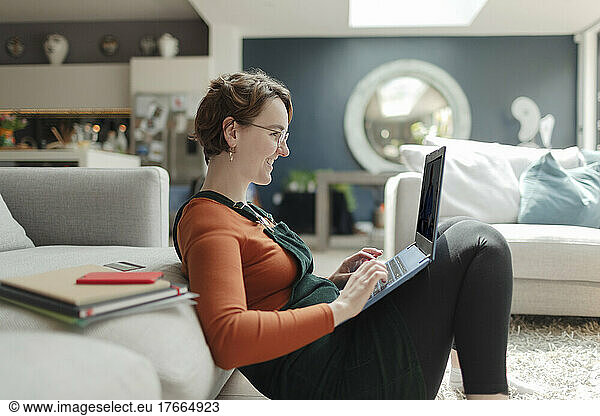 Young woman with laptop working from home in living room
