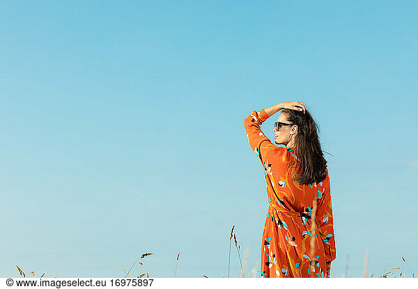 Young woman with long hair and flowery fashion orange dress posing by