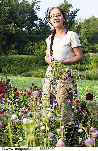 Young woman with long red braid holds freshly-cut flowers in the field