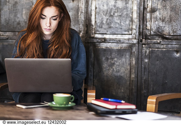 Young woman with long red hair sitting at table  working on laptop computer.