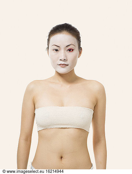 Young woman with opera make-up standing against white background