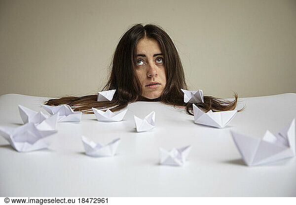 Young woman with paper boats on table in front of wall