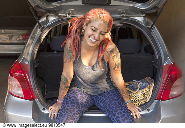 Young woman with pink dreadlocks sitting in boot of car