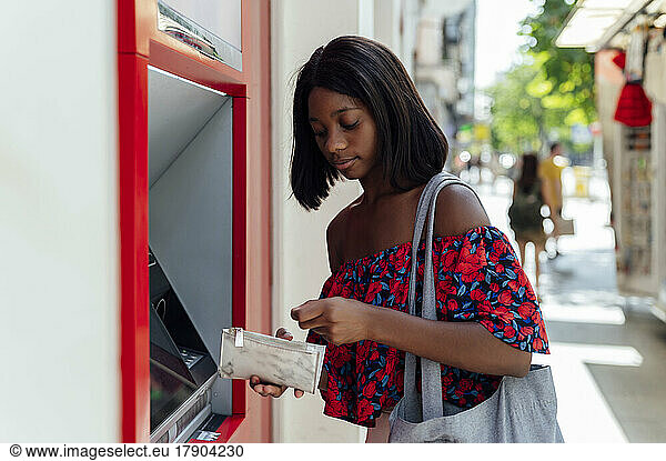 Young woman with purse standing at ATM