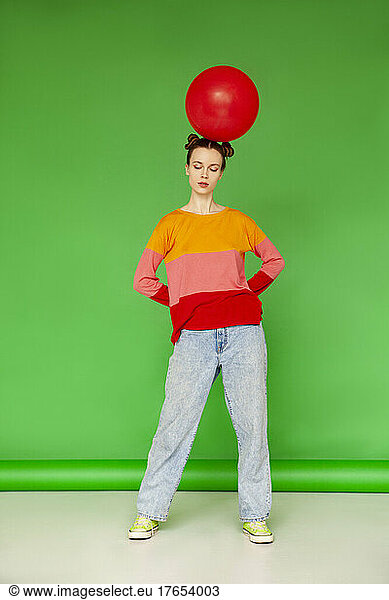 Young woman with red balloon on head standing against green background