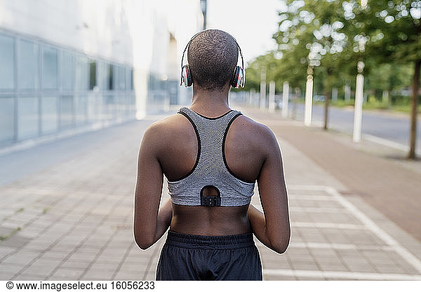 Young woman with shaved head listening music through headphones while standing on footpath