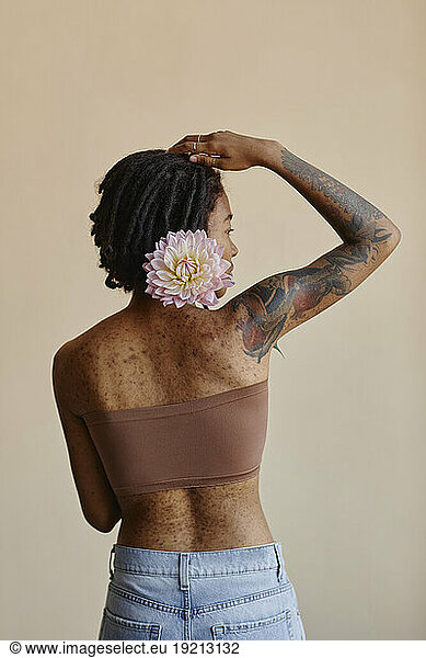 Young woman with short hair holding peony flower against brown background