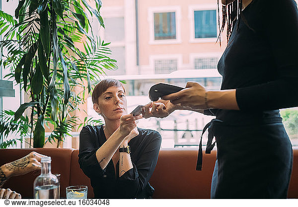 Young woman with short hair sitting in a bar  using credit card to pay.