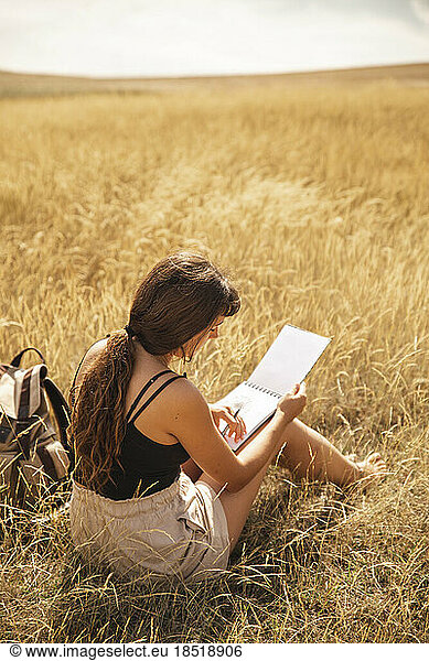Young woman with sketch pad sitting on dry grass