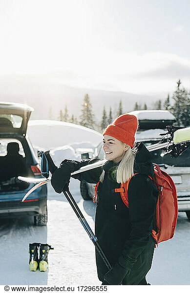 Young woman with skis looking away at parking lot
