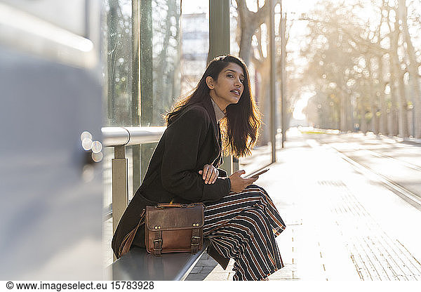 Young woman with smartphone waiting at the tram stop