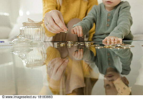 Young woman with son counting coins on table at home