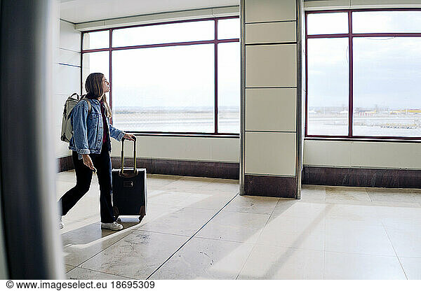Young woman with suitcase walking at airport lobby