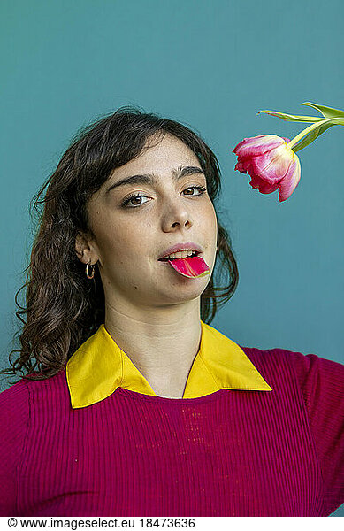 Young woman with tulip petal in mouth against green background