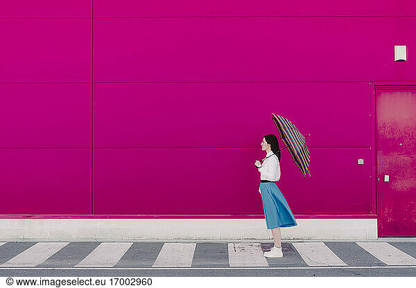 Young woman with umbrella in front of a pink wall