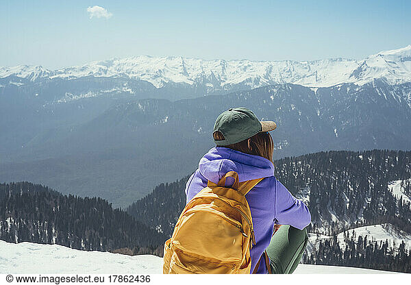 Young woman with yellow backpack sitting in snowy mountains