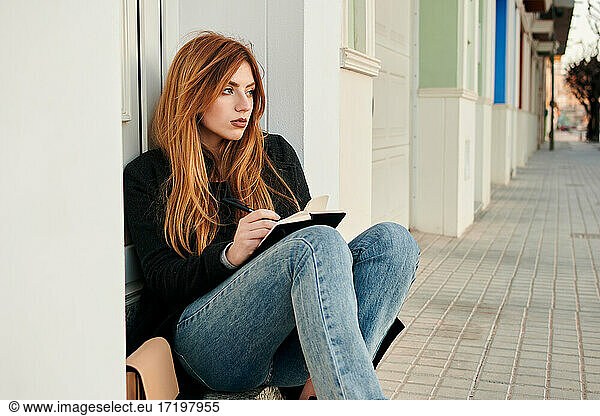 Young woman writes in her notebook while she is sitting on the street