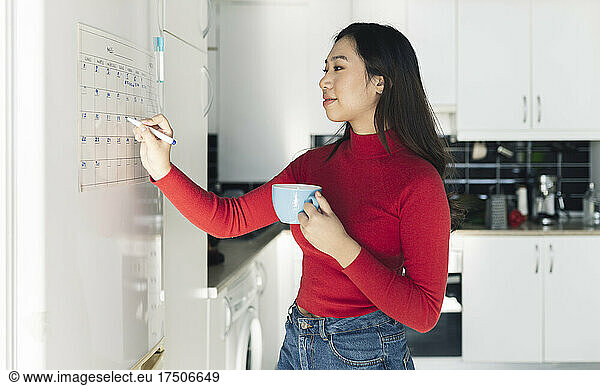 Young woman writing on calendar in kitchen