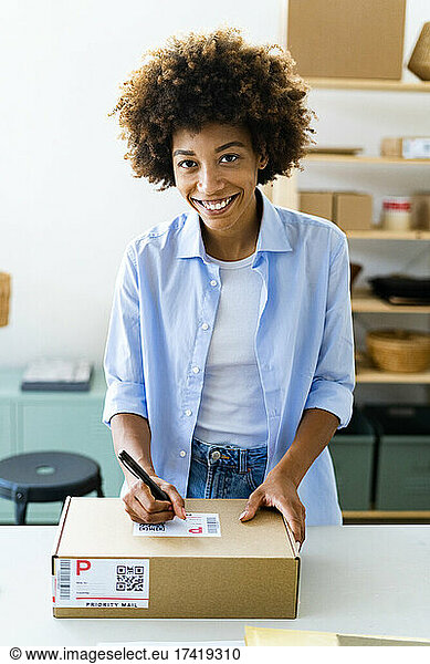 Young woman writing on package at desk in studio